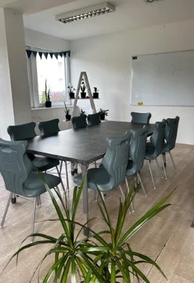 Sala lekcyjna z długim stołem, roślinami i tablicą